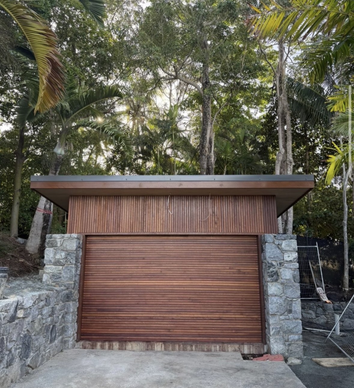 Timber-clad garage between stone walls and established greenery